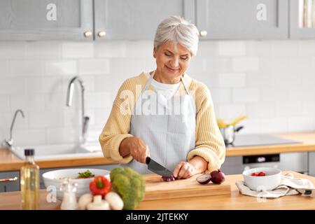 Glückliche Frau hackt rote Zwiebel in der Küche Stockfoto