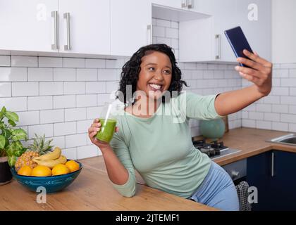 Eine junge multirassische Frau macht ein Selfie mit ihrem grünen Smoothie in der Küche Stockfoto