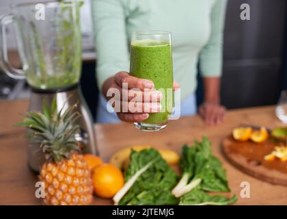 Nahaufnahme der Frauenhand, die zu Hause frisch zubereiteten grünen Smoothie hält Stockfoto