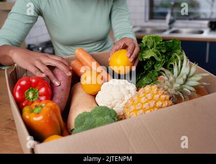 Eine anonyme junge Frau prüft ihre Obst- und Gemüselieferbox Stockfoto