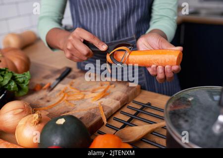 Nahaufnahme der Hände einer jungen Frau, die Karotten für vegane Suppe oder Eintopf schälen Stockfoto