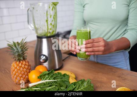 Nahaufnahme einer jungen Frau, die zu Hause frisch zubereiteten grünen Smoothie hält Stockfoto