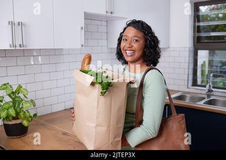 Eine junge Frau aus verschiedenen Rassen kommt mit einer Papiertüte vom Lebensmitteleinkauf nach Hause Stockfoto