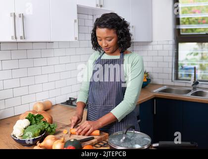 Eine junge multirassische Frau zerkleinert in der Küche Karotten für einen veganen Eintopf Stockfoto