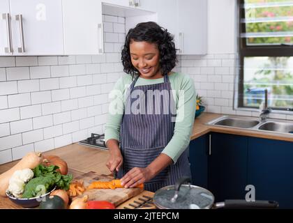 Eine junge Frau aus verschiedenen Rassen zerkleinert in ihrer Küche Karotten zum Abendessen Stockfoto