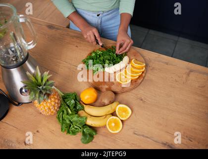 Eine Aufnahme über dem Kopf einer jungen Frau, die Obst und Spinat für grünen Smoothie vorbereitet Stockfoto