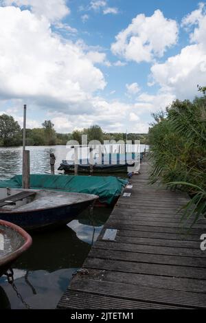 Vertikale Aufnahme von alten verwitterten kleinen Booten, die in einer grünen Gegend mit einem blau bewölkten Himmel festgemacht wurden Stockfoto