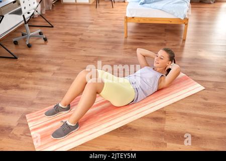 Fröhliches Teenager-Mädchen, das zu Hause auf einer Yogamatte trainiert Stockfoto