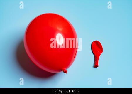 Ein aufgeblähter und ein entlasener roter Luftballon nebeneinander Stockfoto