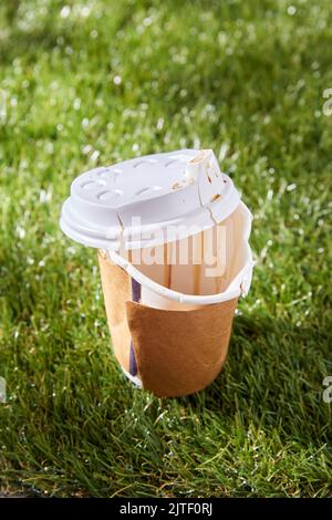 Nahaufnahme der gebrauchten Einweg-Kaffeetasse auf Gras Stockfoto