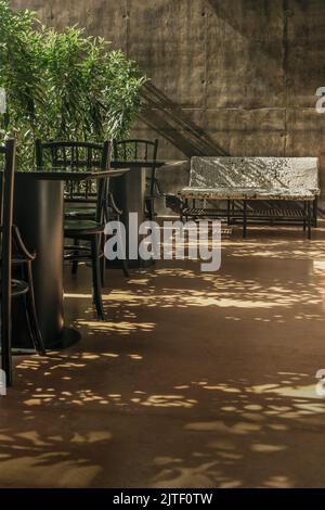 Schöner Sommerblick auf eine leere Café-Terrasse im Sommer mit schwarzen Tischen und Stühlen und Einem weißen Designstuhl aus Tastaturtasten auf Putz. C Stockfoto