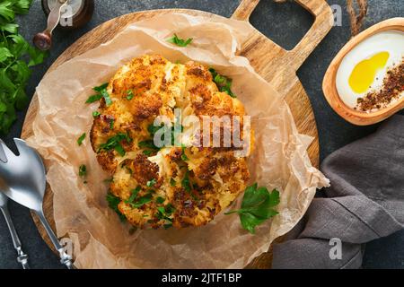 Gebackener Blumenkohl. Ofen oder ganze gebackene Blumenkohl Gewürze und Kräuter Server auf Holz rustikalen Brett auf alten grauen Hintergrund Tisch. Köstlicher Blumenkohl. Stockfoto