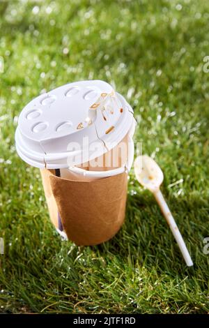 Nahaufnahme der gebrauchten Einweg-Kaffeetasse auf Gras Stockfoto