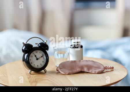 Wecker, Maske und Schlaftabletten auf dem Tisch Stockfoto