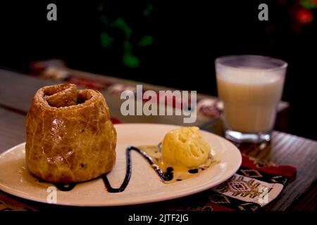 Fultu mit Eis. Blätterteig mit Äpfeln und Nüssen auf einer weißen Keramikplatte und einem Glas Ayran. Krimtatarische Küche. Stockfoto