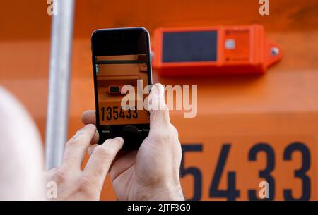 30. August 2022, Hamburg: Ein Mitarbeiter registriert mit einer App auf seinem Smartphone das Live-Tracking-Gerät und die Containernummer auf einem Hapag-Lloyd-Standardcontainer am CMR-Depot (Container Maintenance Repair) im Hafen. Das erste dieser Geräte wird im CMR-Depot der Reederei auf sogenannten Trockencontainern installiert. Bis Ende 2023 wird der Großteil der Container von Hapag-Lloyd in ausgewählten Containerdepots in Nord- und Südeuropa, Asien und dem Nahen Osten mit diesen Geräten ausgestattet. Die Tracking-Geräte übertragen Daten wie Standort und Umgebungstemperatur von e Stockfoto