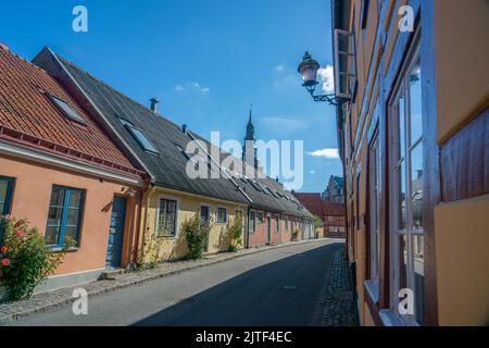 Ystad, Schweden - 24, Aug 2022: Bunte Häuser in einer kleineren Straße in einer kleinen Stadt mit der Spitze der Kirche im Hintergrund Stockfoto