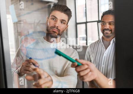 Männer, die im Büro mit Diagrammen auf Glasbrettchen arbeiten Stockfoto
