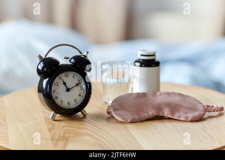 Wecker, Maske und Schlaftabletten auf dem Tisch Stockfoto