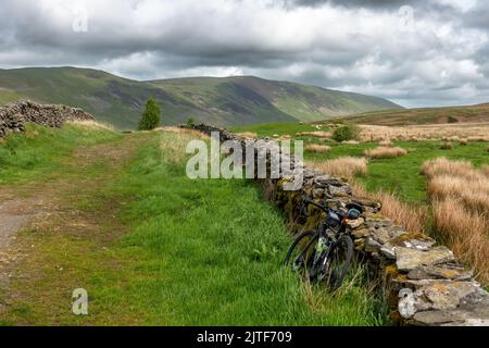 Fahrrad, das sich an einer alten Steinmauer auf einem Reitweg nach Norden in Richtung Calf Top Fell und Caslte Knot, Cumbria, Yorkshire Dales National Park lehnt, Stockfoto