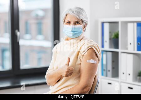 Geimpfte Frau in Maske mit medizinischem Pflaster am Arm Stockfoto