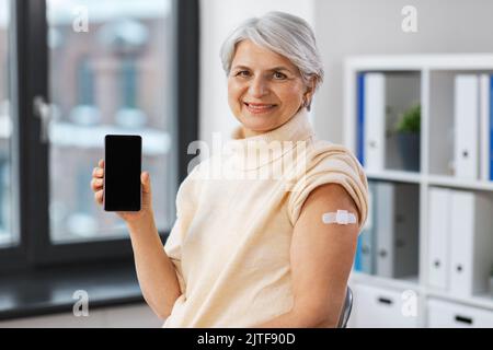 Lächelnde Frau mit medizinischem Pflaster am Arm und am Telefon Stockfoto
