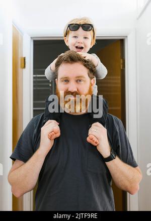 Das Porträt eines Vaters, der seinen Sohn (2-3) zu Hause auf den Schultern trägt Stockfoto