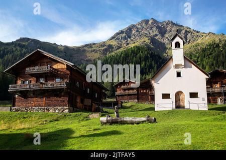 Weiße Kirche und Holzhütten eines Oberstalleralmdorfes in Innervillgraten, Villgratental, Osttirol, Tirol, Österreich Stockfoto