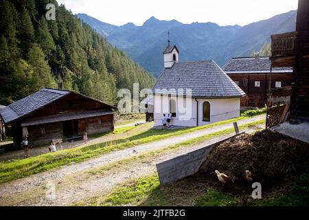 Weiße Kapelle und Holzhütten in einem Dorf der Oberstalleralm in den österreichischen alpen, Innervillgraten, Villgratental, Osttirol, Tirol, Österreich Stockfoto