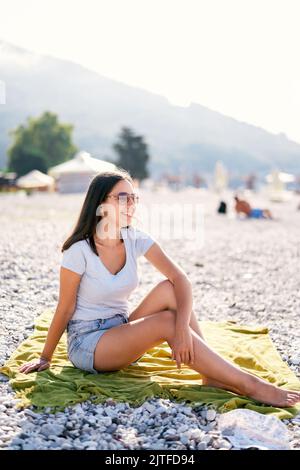 Junge lächelnde Frau sitzt auf einer Decke am Strand Stockfoto