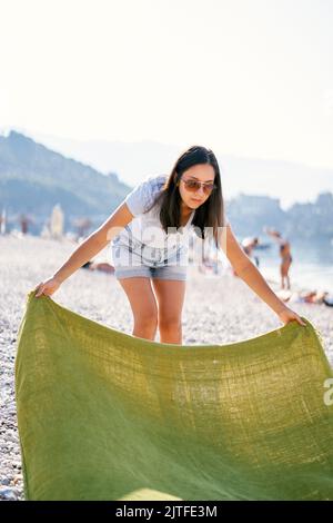Eine junge Frau breitet eine Decke auf einem Kiesstrand aus Stockfoto