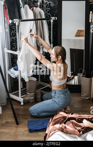 Schrank organisieren, Schrank entkleiden. Junge Frau entrümpelt Kleiderschrank und Wahl Kleidung im Schlafzimmer Stockfoto