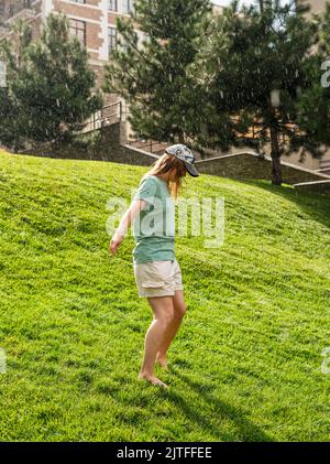 Glückliche junge Frau barfuß auf grünem Rasen spazieren und den warmen Regen im Sommer genießen und das Naturgefühl genießen Stockfoto