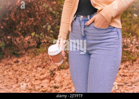 Papierglas Kaffee in der Hand auf dem orangefarbenen Herbstlaub Hintergrund Stockfoto