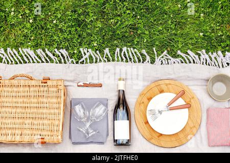 Korb, Geschirr und Weinflasche auf Picknickdecke Stockfoto