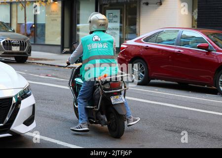 Eine fantuanische Person, die Lebensmittel auf einem elektrischen Moped in New York City geliefert hat. 飯糰外賣 Food Delivery Gig worker. Stockfoto