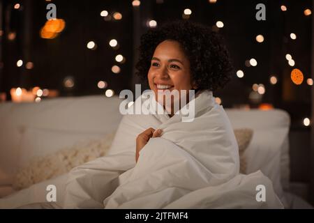 Frau in Decke gewickelt, die nachts im Bett saß Stockfoto