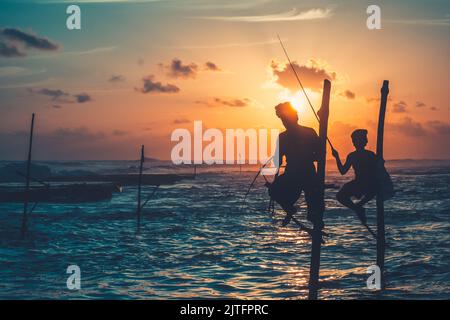 Sri Lanka zwei lokale Fischersilhouetten am Sonnenuntergangsmeer. Traditionelle Fischer, die am Stock fischen - berühmte Touristenattraktion. Beeindruckende, helle und farbenfrohe Meereslandschaft. Reisen, Abenteuer, Konzeptbild. Stockfoto