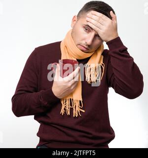 Ein Mann hält seine Hand wegen Kopfschmerzen auf dem Kopf, ein Porträt eines Mannes auf weißem Hintergrund, der Hals eines Mannes ist in einen Schal gewickelt. Stockfoto