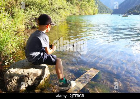 Ein kleiner Junge auf dem See steuert ein Spielzeugboot Stockfoto