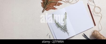 Getrocknetes gepresstes Blatt auf Papier aus Notizbuch mit Bleistift, Schere und Garn auf weißem Hintergrund. Hobby, handgemachte, florale Kunst und Boho Concept Banner Stockfoto