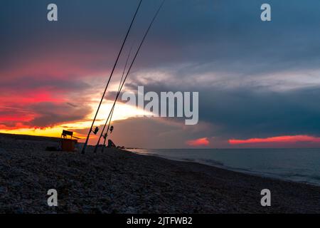 Angelruten am Ufer des Meeres vor dem Hintergrund eines dramatischen Sonnenuntergangs. Wunderschöner Sonnenuntergang über dem Meer. Nachtfischen. Stockfoto