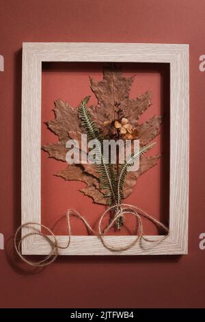 Bouquet aus getrockneten gepressten Blatt in Rahmen auf braunem Hintergrund. Hobby, handgemachte, florale Kunst und boho Stil Konzept. Stockfoto