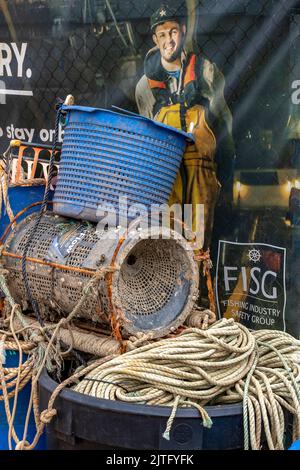 Plakat für die Sicherheit der Fischer auf See auf Trawlern mit alten abgelegten Netzen und Töpfen im Vordergrund, die das Plakat teilweise blockieren, Ironie. Stockfoto