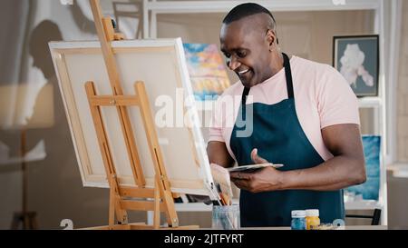 Seitenansicht glücklich lächelnd fröhlich kreativ talentiert inspiriert alten afroamerikanischen Senioren Künstler männlichen Maler in Schürze Zeichnung Bild Stockfoto