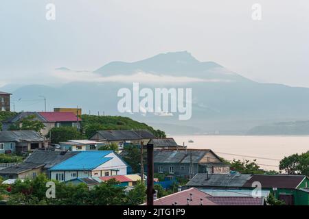 Landschaft der Stadt Yuzhno-Kurilsk auf der Insel Kunashir mit Blick auf die Meeresbucht und den Mendelejew-Vulkan in der Ferne Stockfoto