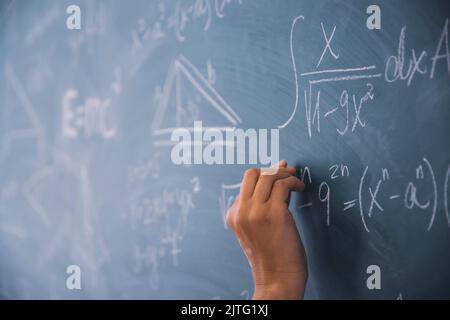 Nahaufnahme einer Hand, die Kreide hält und mathematische Gleichungen auf die Tafel schreibt. Bildungskonzept. Stockfoto