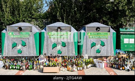 Newport, Pembrokeshire, Wales - August 2022: Viele Weinflaschen, die neben voll gefüllten Recyclingbehältern zurückgelassen wurden Stockfoto