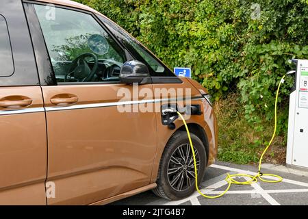 Newport, Pembrokeshire, Wales - August 2022: Elektrofahrzeug an eine Ladestation im Dorfparkplatz angeschlossen Stockfoto