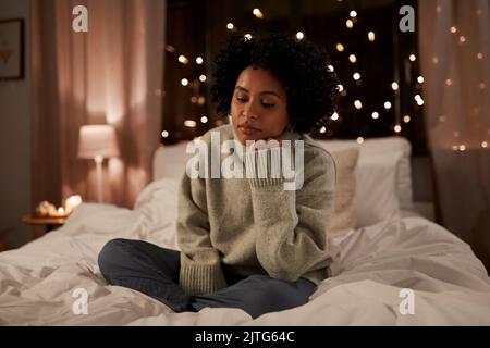 Traurige Frau im Pullover auf dem Bett zu Hause in der Nacht Stockfoto